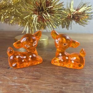 Pair of vintage 1970s amber orange translucent plastic Bambi fawn deer figurines on wooden surface.