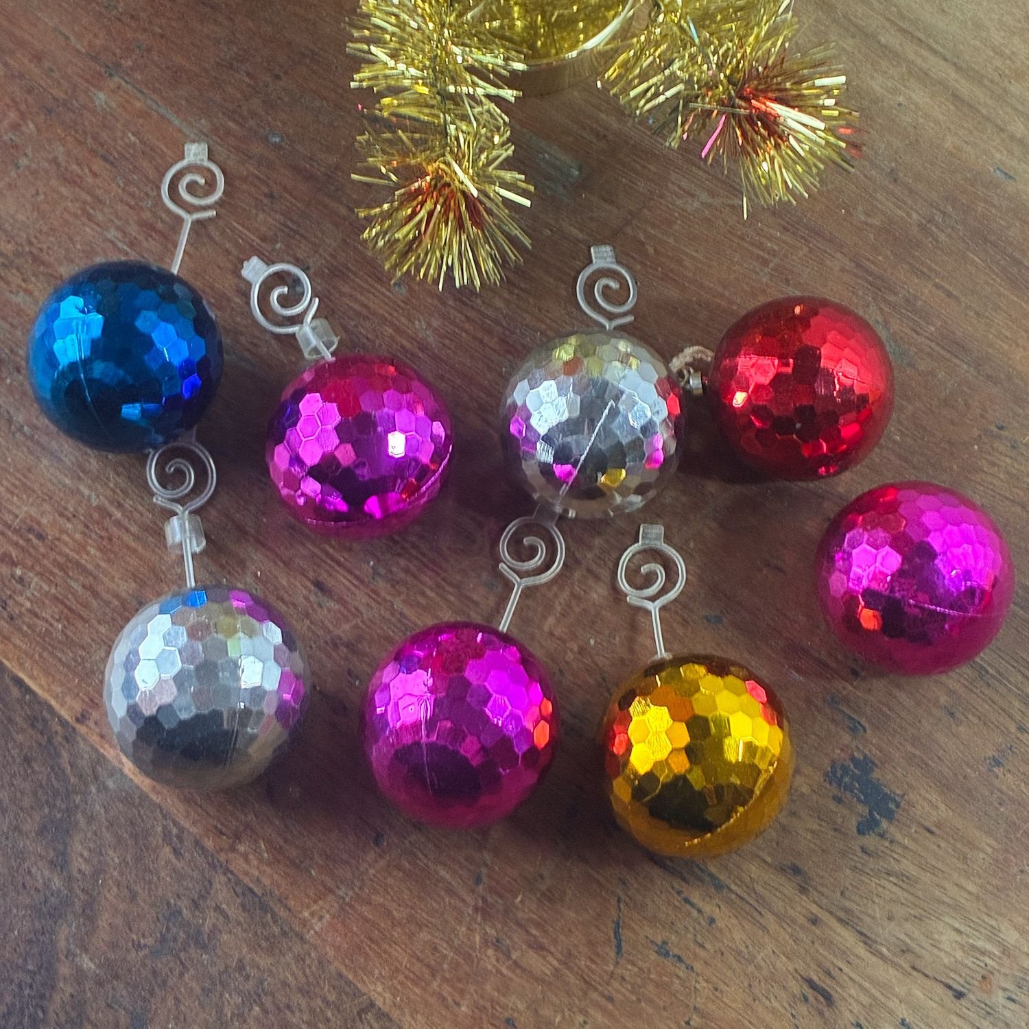 Set of eight colorful 1970s faceted metallic disco ball Christmas baubles arranged on wooden table.