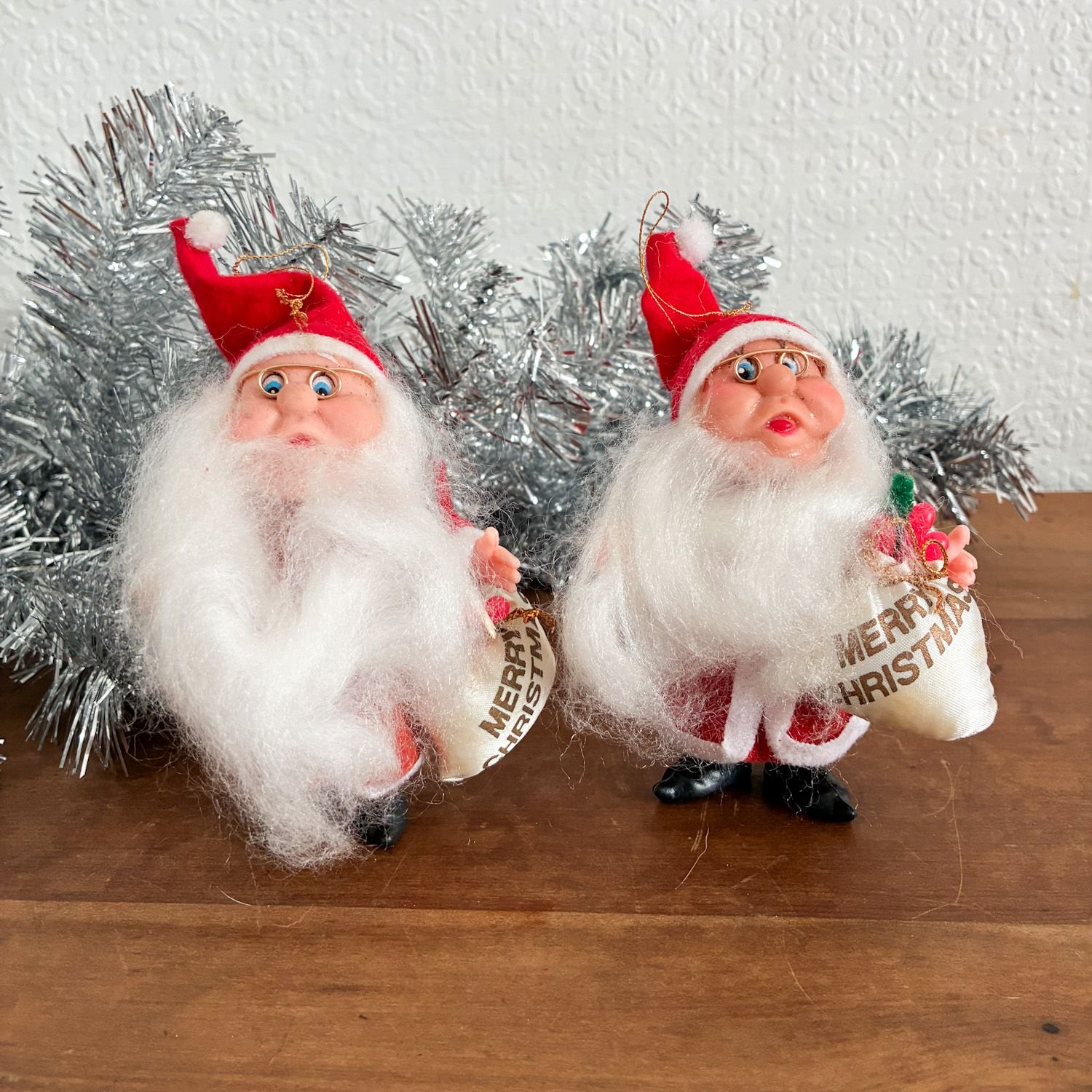 Pair of vintage 1980s red flock Santa Claus gnome tree ornaments with wire glasses and Merry Christmas sacks.