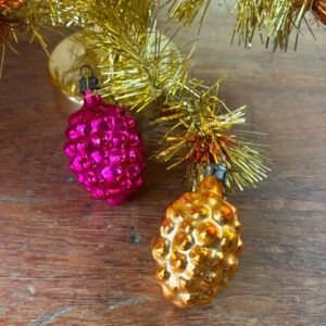 ⁠Pair of vintage pink and gold mercury glass pinecone Christmas baubles on wooden surface.