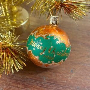 Vintage 1988 gold glass Christmas bauble with green Merry Christmas 1988 inscription hanging on tinsel.